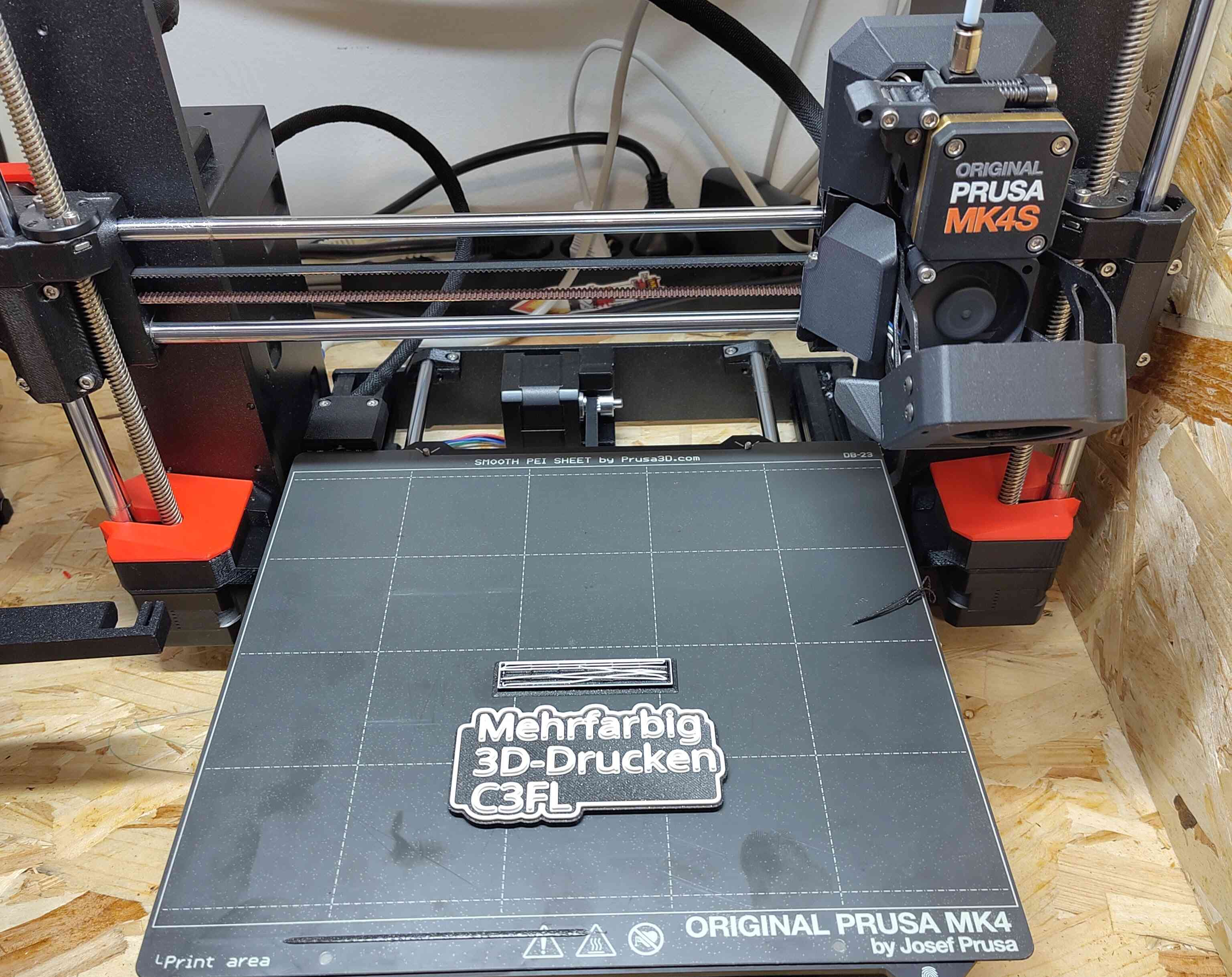 3D-Gedrucktes Schild auf dem steht: Mehrfarbig 3D-Drucke C3FL mit weißem Text und Schwarzen hintergrund auf einem Prusa MK4S