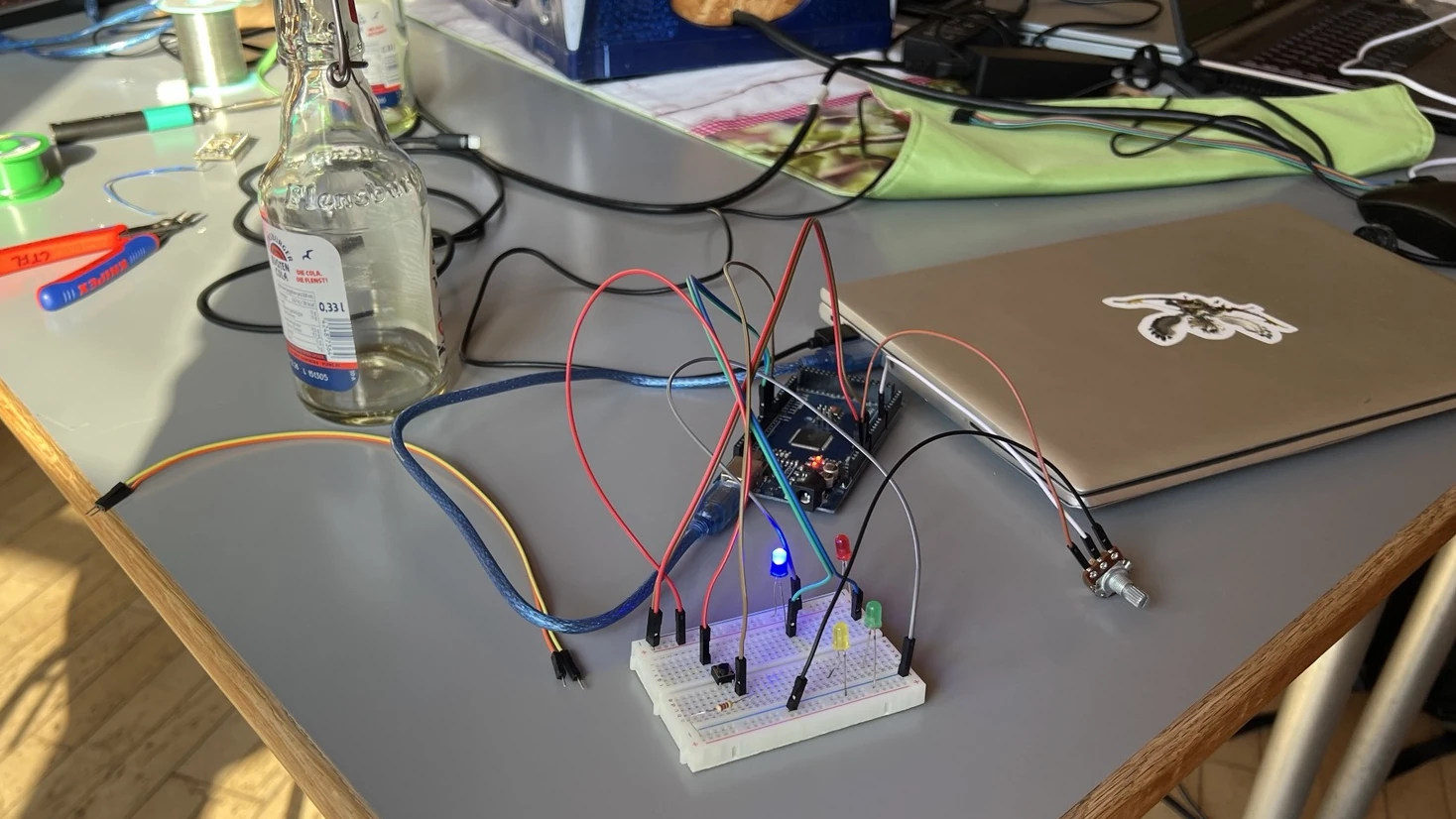Auf einem Schreibtisch steht ein Laptop, an welchem ein Arduino MEGA mit vier LEDs und einem Potentiometer angeschlossen ist